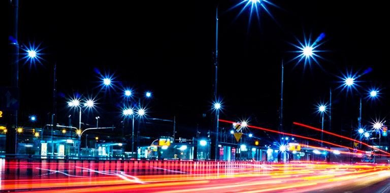 Cidade de noite com as luzes dos postes acesas e luzes de carros que passaram
