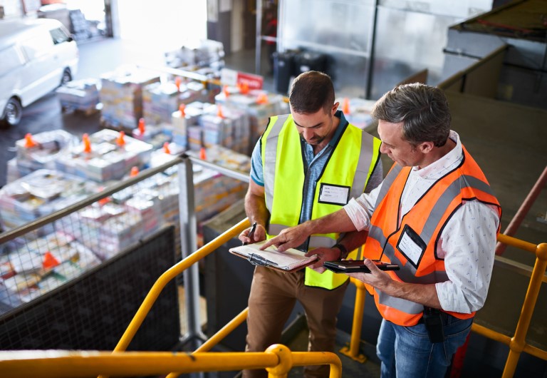 Shot of two warehouse workers standing on stairs using a digital tablet and looking at paperwork