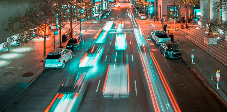 Cidade de noite com as luzes dos postes acesas e luzes de carros que passam
