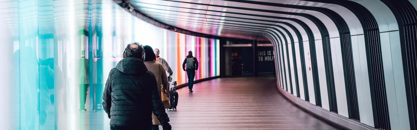 Corredor de um  edifício com pessoas passando e bem iluminado.