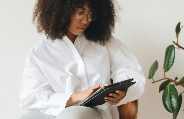 Mulher negra de óculos, segurando um tablet e olhando pra ele