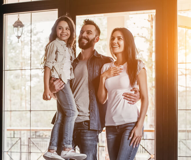 Família sorrindo na porta de casa do lado de dentro
