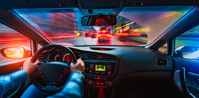 Veículo visto de dentro, de noite com as luzes da cidade e dos outros carros.