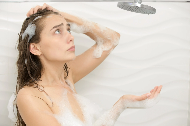 Mujer preocupada en la ducha porque no le cae agua, debido a una emergencia en el hogar.
