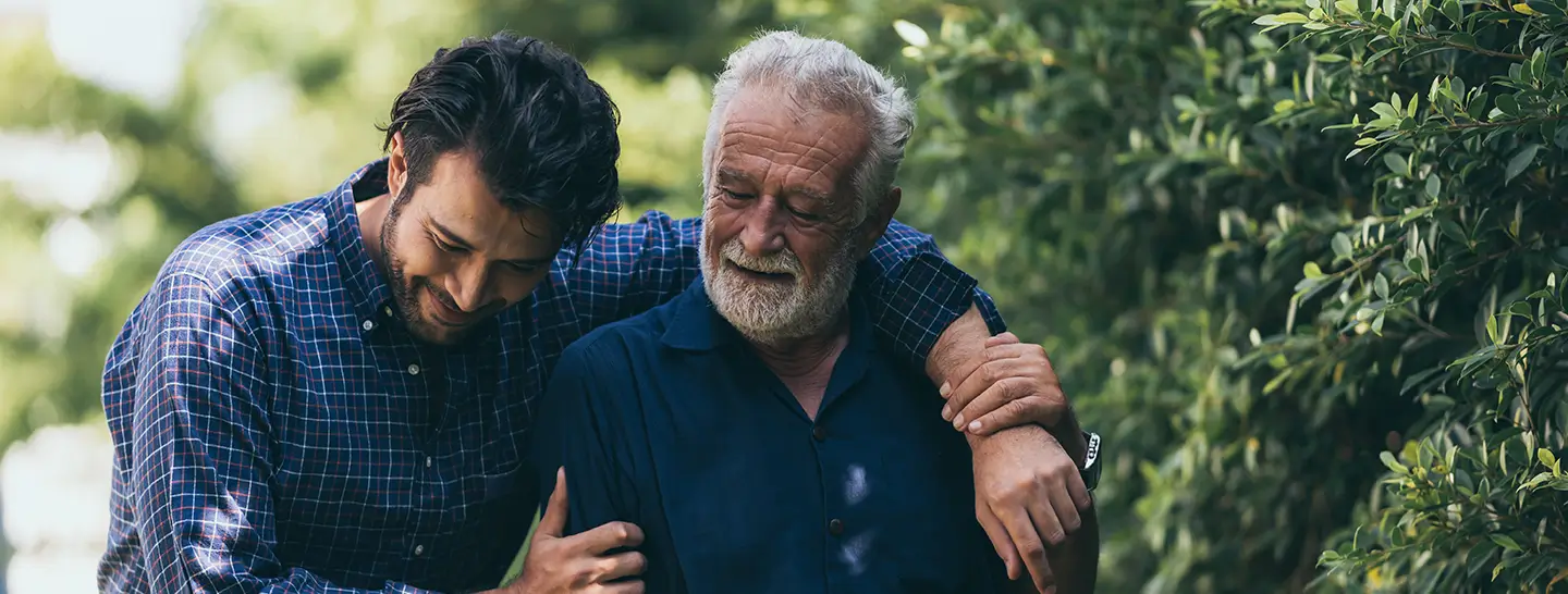 Padre e hijo paseando por un parque abrazados, después al revisar las características del plan de Asistencia Funeraria de Enel X.