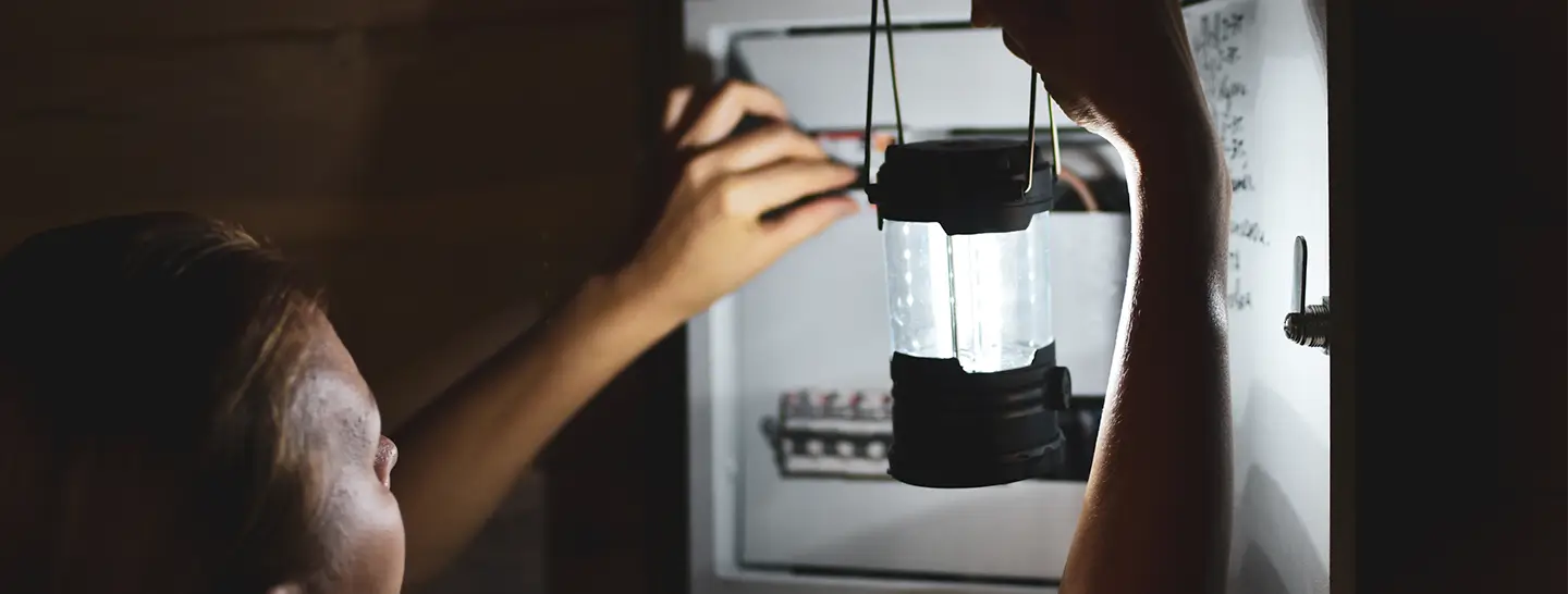 Mujer con una emergencia eléctrica en casa, revisando con linterna la caja de fusibles