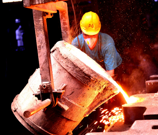 Foundry worker pouring molten metal from a ladle in an industrial facility