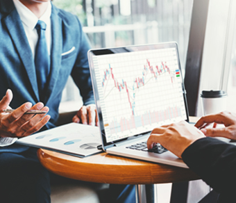 Due uomini d'affari seduti ad un tavolino lavorano su dati statistici al computer