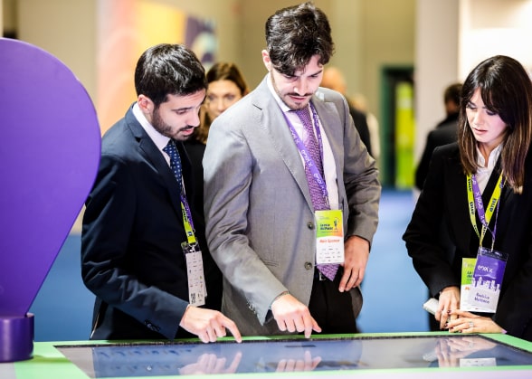 Visuale dello stand di Enel X ad ANCI, tre persone consultano il touch screen