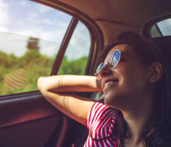 Donna rilassata e sorridente seduta sui sedili posteriore di un'auto in movimento.