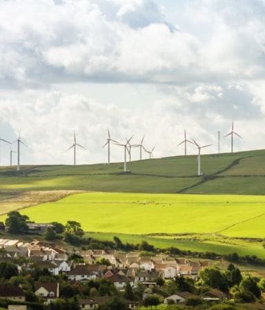  wind turbines on a hillside overlooking housing