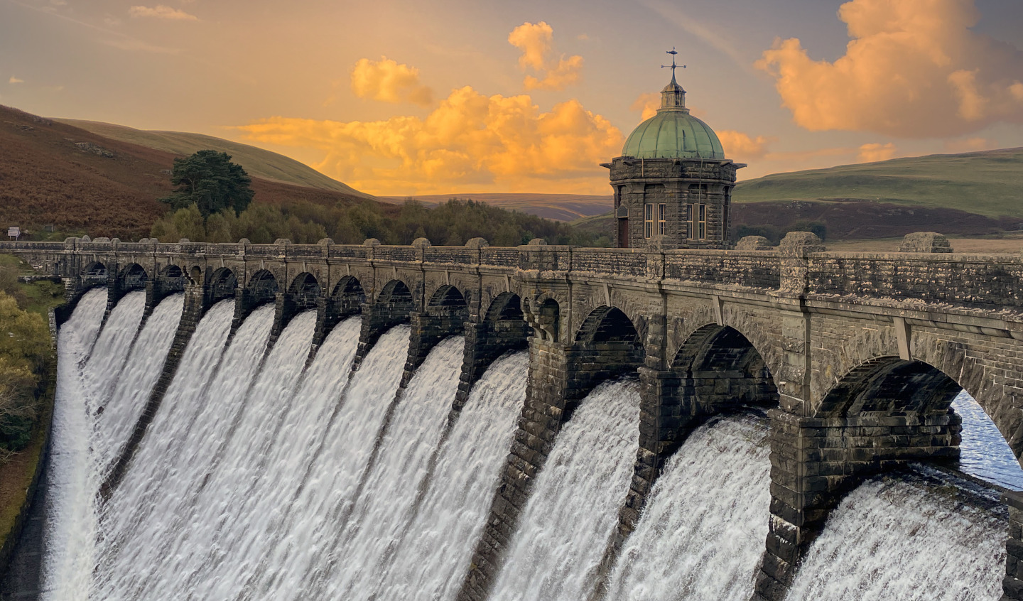 Hydroelectric dam with water flowing over the spillway at sunset